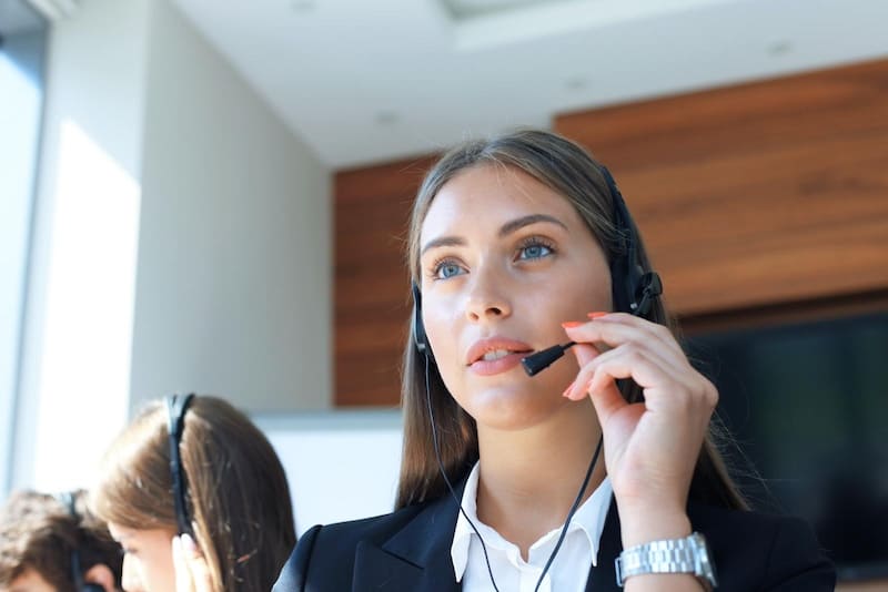 A professional wearing a headset and business attire in a modern office setting, focused on a customer service call with wood paneling visible in the background.
